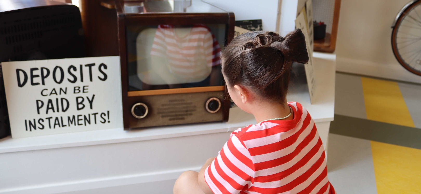 A child sat in front of a TV in the showroom at a Reece Ltd Radio and Electrical services shop at Beamish Museum