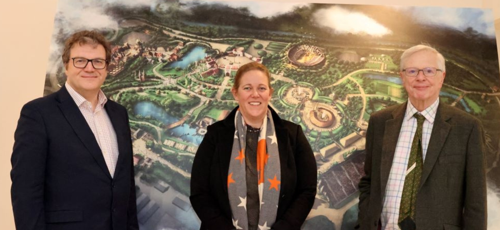 Three people standing in front of the plans for Kynren's theme park